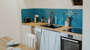 Une cuisine de taille réduite, avec une table en bois, des chaises blanches, un évier, un lave-vaisselle et une cuisinière.