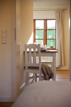 Ein Zimmer mit einem weißen Stuhl, einem Tisch und einem Fenster mit Vorhängen.