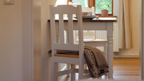 Une pièce avec une chaise blanche, une table sur laquelle se trouvent une assiette et une tasse, une fenêtre avec des rideaux et un radiateur.