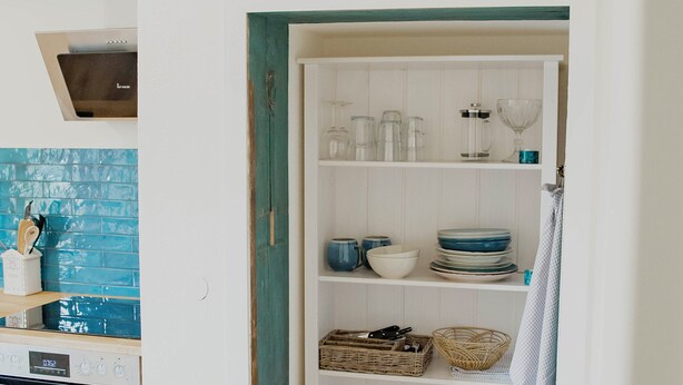 Une cuisine équipée d’une cuisinière, d’un four et d’étagères où sont rangés la vaisselle et les ustensiles de cuisine.