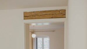 Une chambre avec un plancher en bois, un lit, une chaise blanche et une fenêtre avec des rideaux.