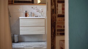Une salle de bain avec un meuble-lavabo blanc, un miroir, un luminaire et une poubelle.