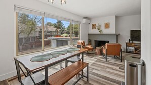 A modern kitchen with a dining area, large windows, and a fireplace.