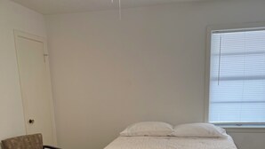 Makuuhuoneessa on sänky, tuoli, kattotuuletin ja ikkuna, jossa on sälekaihtimet.