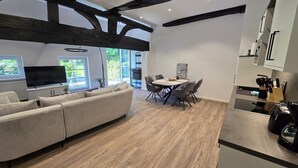Una sala de estar moderna con un sofá seccional, una mesa de comedor con sillas y una cocina con armarios y electrodomésticos.