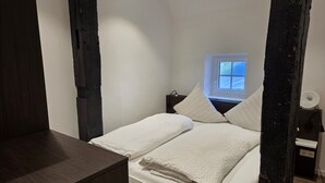 Una habitación pequeña y funcional con cama, mesita de noche, ventana y velador.