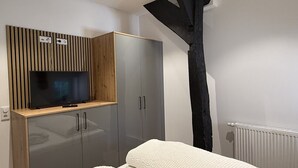 Een slaapkamer met een bed, een tv bevestigd aan een houten kast, een kledingkast en een radiator.