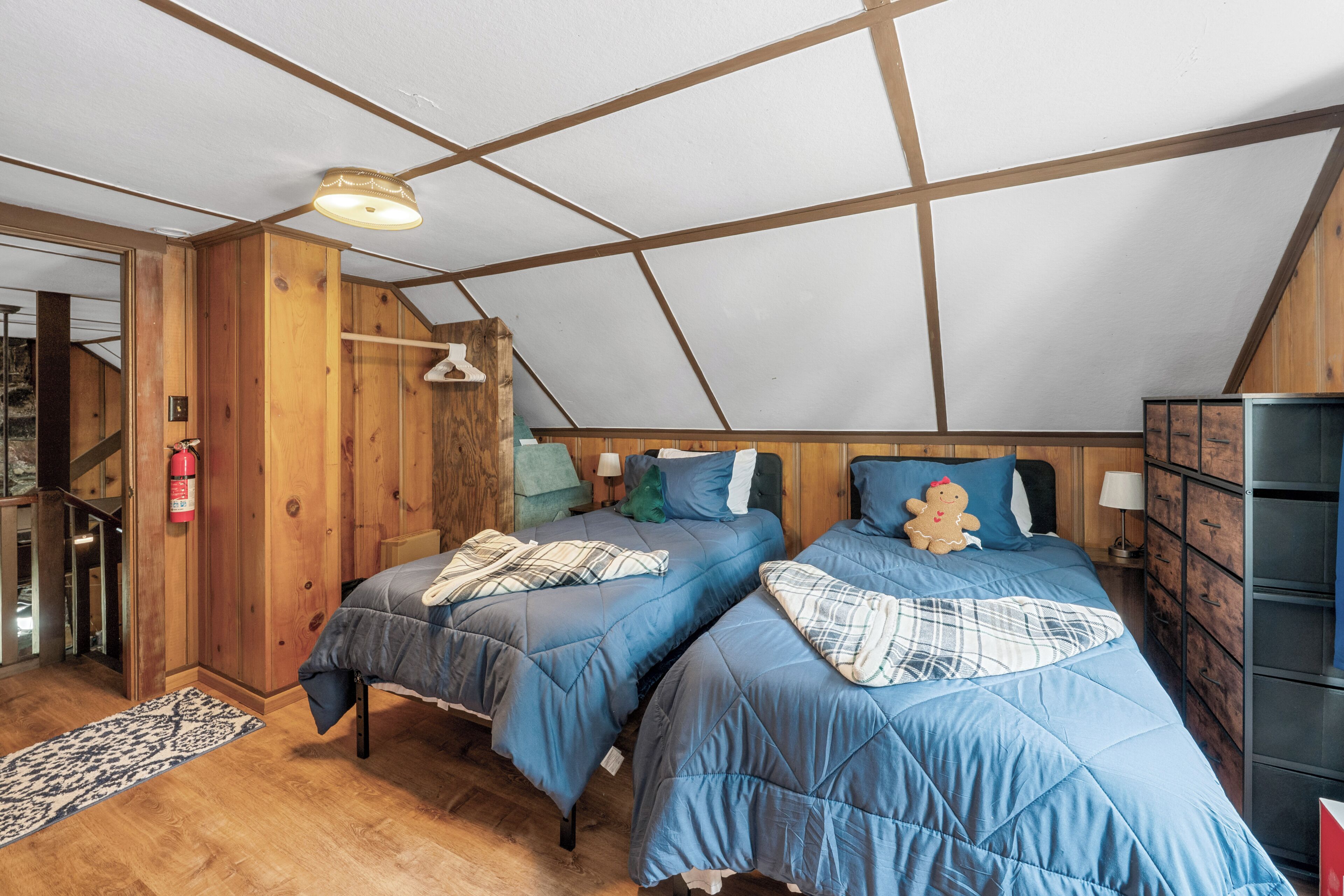 A bedroom with two beds, wooden walls, a sloped ceiling, and a small staircase.