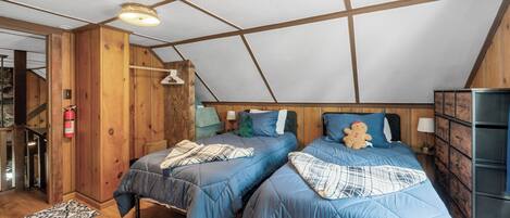 A bedroom with two beds, wooden walls, a sloped ceiling, and a small staircase.