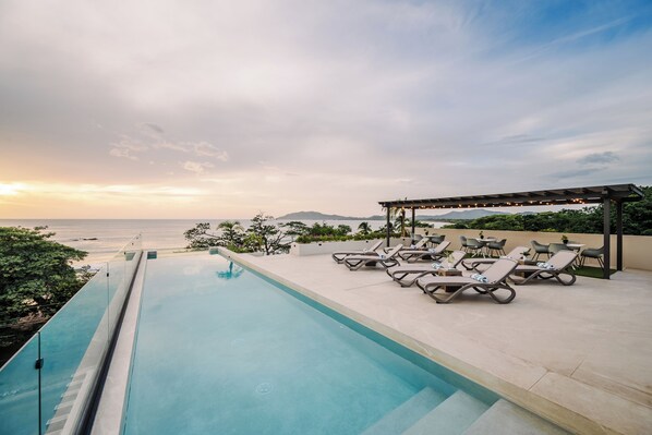 A poolside area with lounge chairs and a pergola, overlooking a body of water. - Iguana Surf Boutique Hotel Tamarindo (Tamarindo)