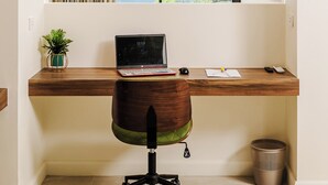 A workspace with a laptop, a chair, a small plant, and a view of the sea through a window. - Iguana Surf Boutique Hotel Tamarindo (Tamarindo)