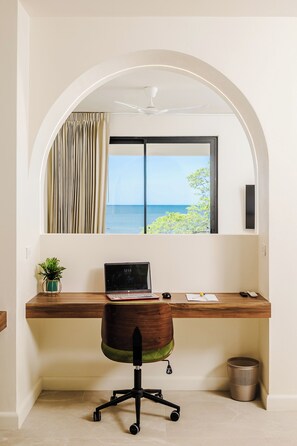 Un espacio de trabajo con un ordenador portátil, una silla, una pequeña planta y vistas al mar a través de una ventana.