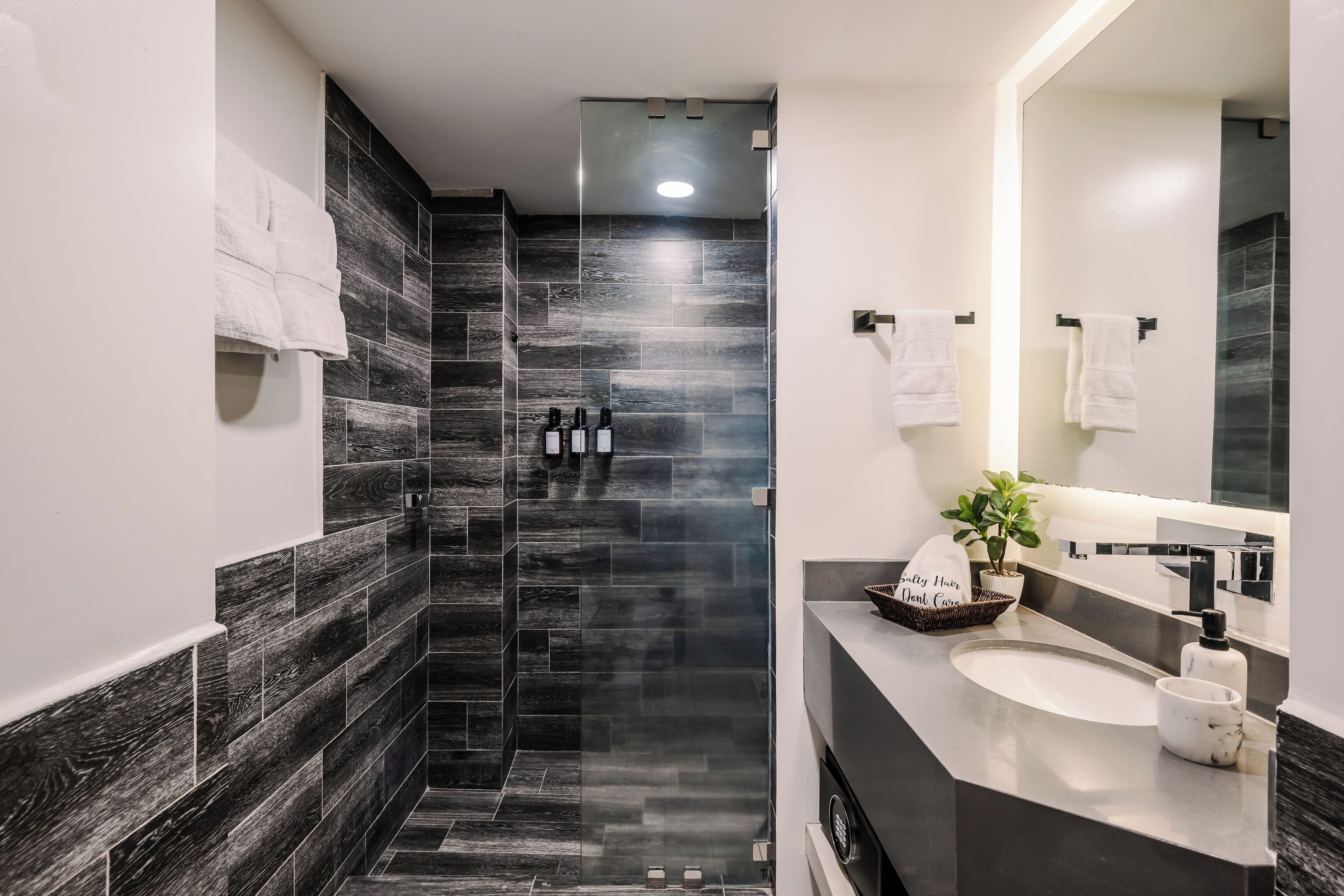 A modern bathroom with a glass shower enclosure, a sink with a marble countertop, and a large mirror.
