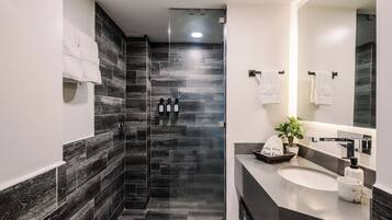 A modern bathroom with a glass shower enclosure, a sink with a marble countertop, and a large mirror.