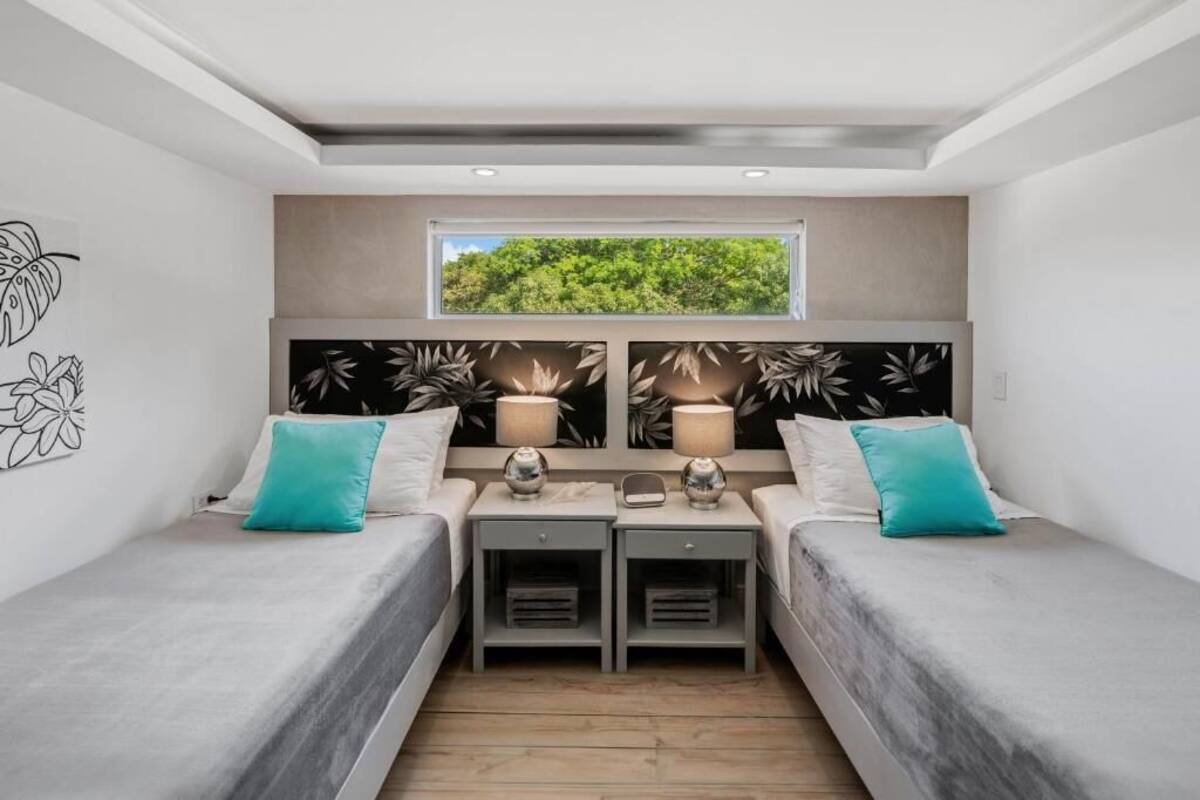 A bedroom with two single beds, a window with a view of greenery, and a wall with abstract art.