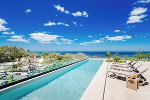 A pool with a view of the ocean, lounge chairs, and a clear sky. - Iguana Surf Boutique Hotel Tamarindo (Tamarindo)