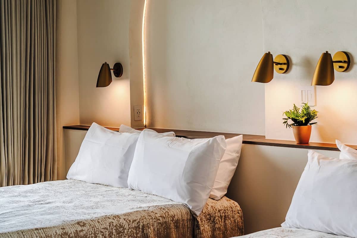 A hotel room with two beds, a potted plant, and wall-mounted lighting fixtures.