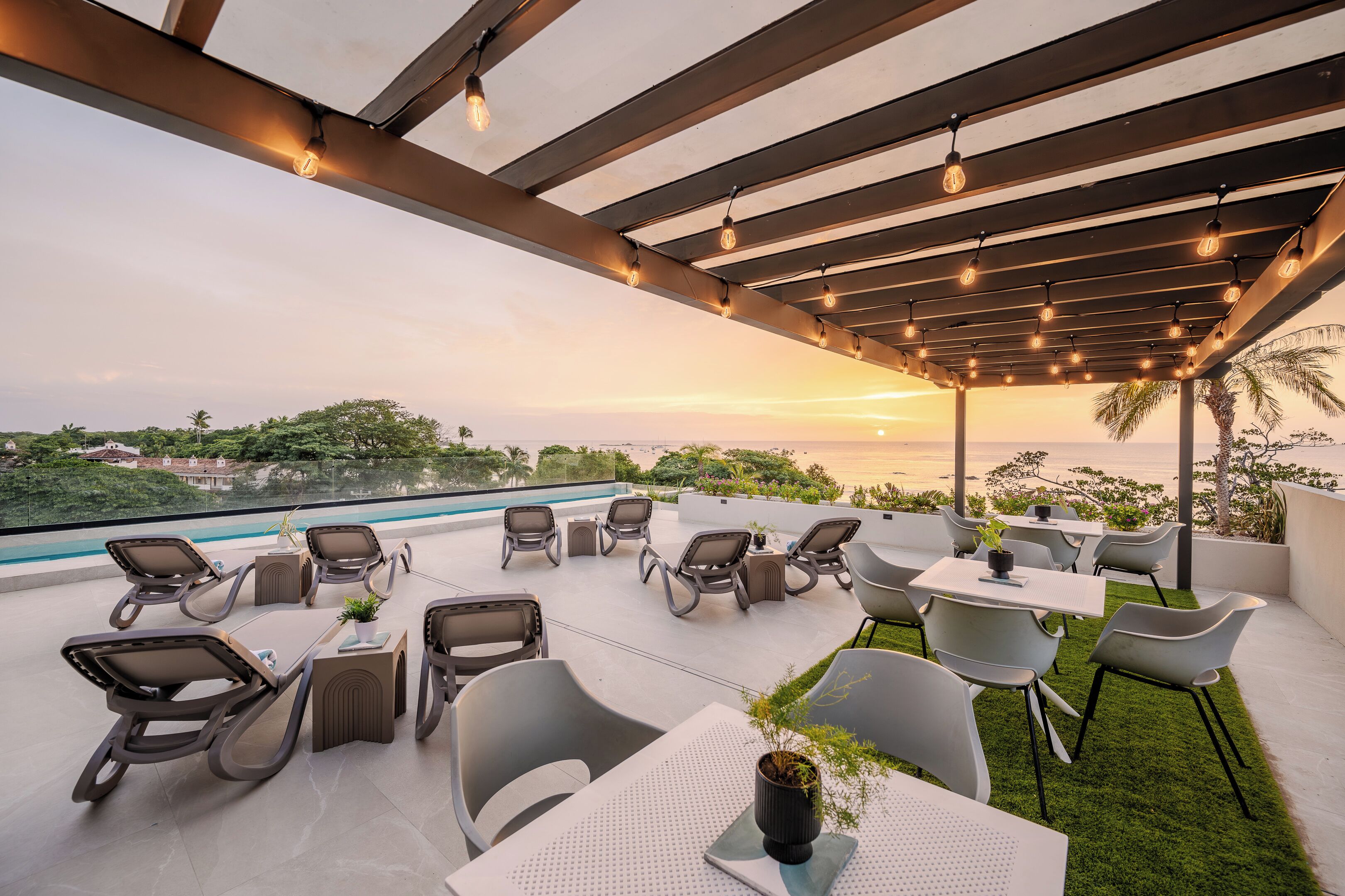 Eine Dachterrasse mit Sitzgelegenheiten im Freien, einem Pool und Blick auf das Meer bei Sonnenuntergang.