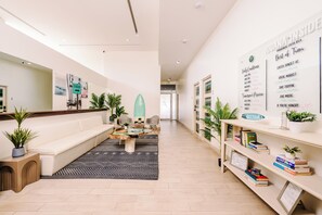 A modern hotel lobby with a sofa, coffee table, and a wall displaying daily conditions and activities. - Iguana Surf Boutique Hotel Tamarindo (Tamarindo)