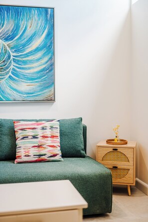 A room with a green sofa, a colorful pillow, a wooden side table with a basket, and a wall-mounted painting. - Iguana Surf Boutique Hotel Tamarindo (Tamarindo)
