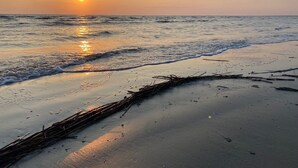 A beach with the sun setting over the ocean, waves gently lapping at the shore, and driftwood on the sand. - Harbor Hideaway …just steps to the beach and pool! (Harbor Island)