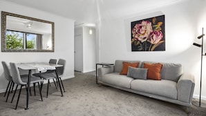 A modern living room with a dining area, a grey sofa, a painting, and a floor lamp. - Comfortable Stay Near Melbourne's West End (Melbourne)