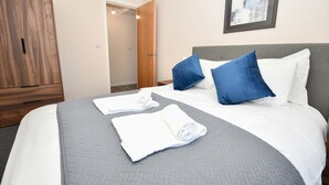 A hotel room with a bed, pillows, a wardrobe, and a door leading to another room. - Bright & Spacious 2 Bed Apartment in Manchester (Manchester)