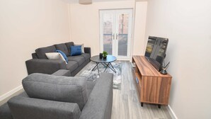 A modern living room with a grey sofa, a coffee table, and a wooden TV stand. - Bright & Spacious 2 Bed Apartment in Manchester (Manchester)