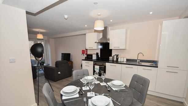 A modern kitchen with white cabinets, a dining table set for four, and a living area with a sofa and a TV. - Bright & Spacious 2 Bed Apartment in Manchester (Manchester)