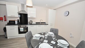 A modern kitchen with white cabinets, a black countertop, and a dining area set for four with a round table and four chairs. - Bright & Spacious 2 Bed Apartment in Manchester (Manchester)