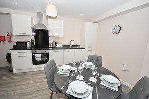 A modern kitchen with white cabinets, a black countertop, and a dining area set for four with a round table and four chairs. - Bright & Spacious 2 Bed Apartment in Manchester (Manchester)