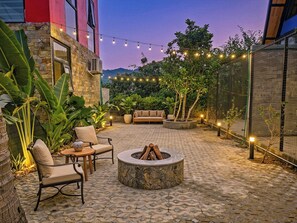 A courtyard with a stone fire pit, outdoor seating, string lights, and lush greenery. - Cat Ba Fishing Village Bay House (Cat Ba Island)