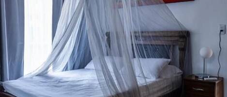 A bedroom with a bed under a canopy, a bedside table, a wall-mounted air conditioner, and a painting.
