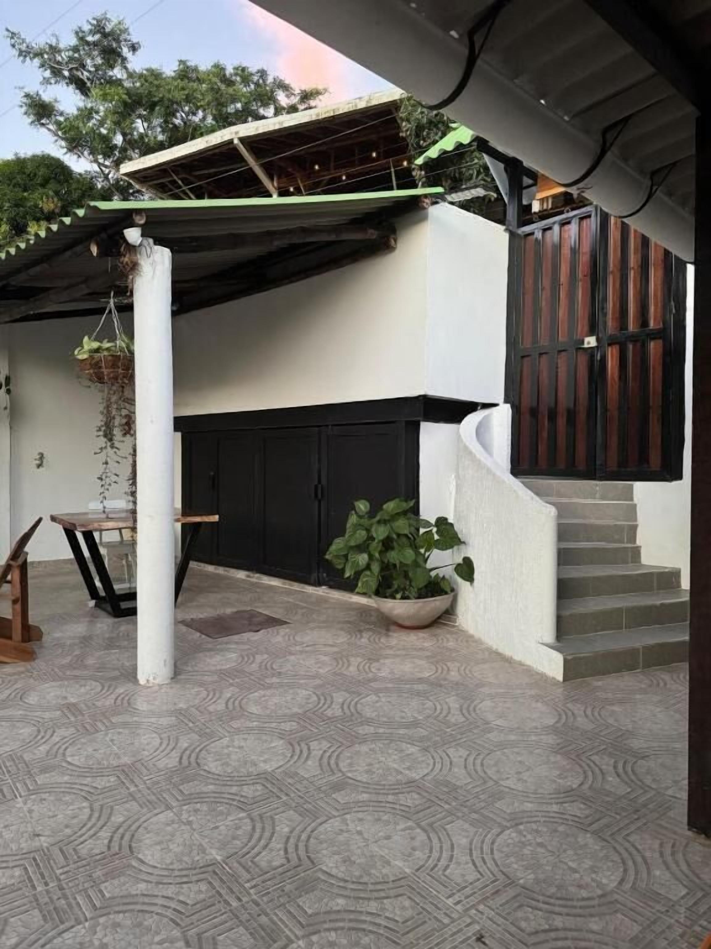 A covered outdoor area with a staircase leading to a second floor, a potted plant, and a hanging plant.