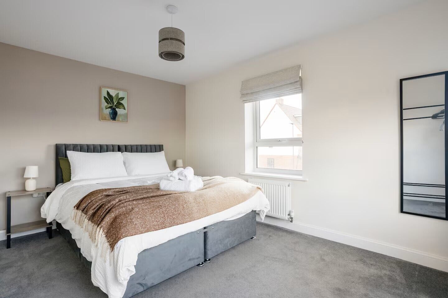A bedroom with a bed, bedside table, lamp, window, radiator, and a plant.