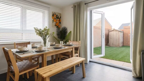 A dining area with a wooden table, chairs, and a bench. There is a window with blinds, a painting on the wall, and a view of a backyard with a wooden shed. - Modern 4BR Home 10 Beds Family-Friendly, Aylesbury (Bierton)