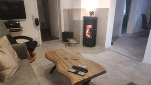 Ein Wohnzimmer mit Couch, Fernseher, Kamin und einem Holz-Couchtisch, im Hintergrund eine Küche.