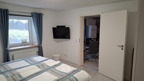 Ein Schlafzimmer mit Bett, Fernseher, einem Fenster mit Vorhängen, einer Heizung und einer Tür zu einem Badezimmer.