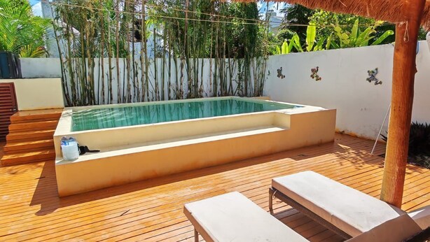 Un espace piscine doté d’une terrasse en bois, de chaises longues et d’un toit de chaume.