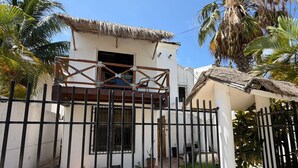 Un bâtiment blanc avec un toit de chaume, un portail en métal et une cour dallée agrémentée de palmiers.