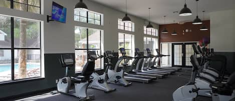 Ein Fitnessstudio mit Laufbändern, Ergometer und einem Fernsehbildschirm.