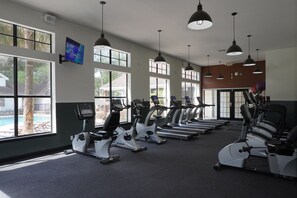 Une salle de sport équipée de tapis de course, de vélos d’appartement et d’un écran de télévision.