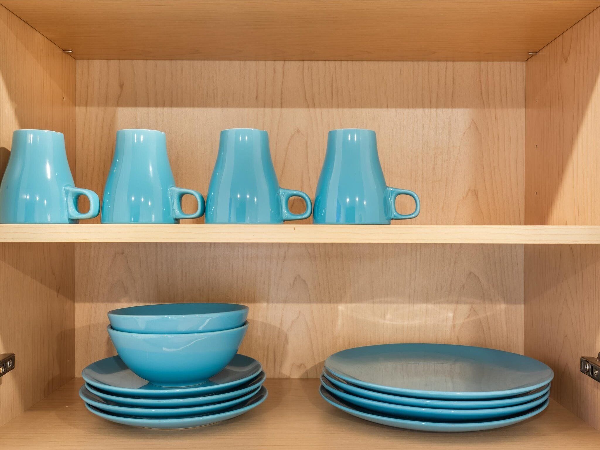 A wooden cabinet with shelves holding blue ceramic mugs and bowls.