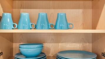 A wooden cabinet with shelves holding blue ceramic mugs and bowls.