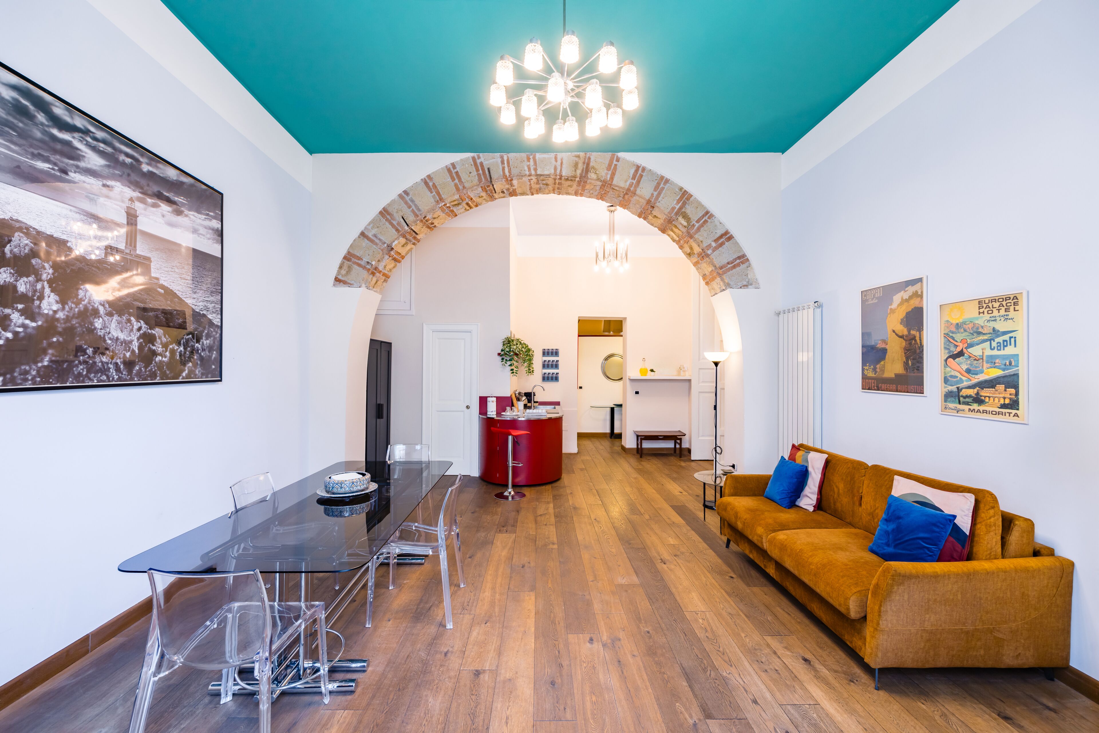 Uma sala de estar moderna com uma mesa de jantar de vidro, um sofá e uma área de cozinha visível através de um arco.