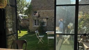 A modern kitchen with a large window, a wooden table, and a cozy seating area. - Charming stone house in the heart of the Vexin, enclosed garden and view of the bell tower (Vaudancourt)