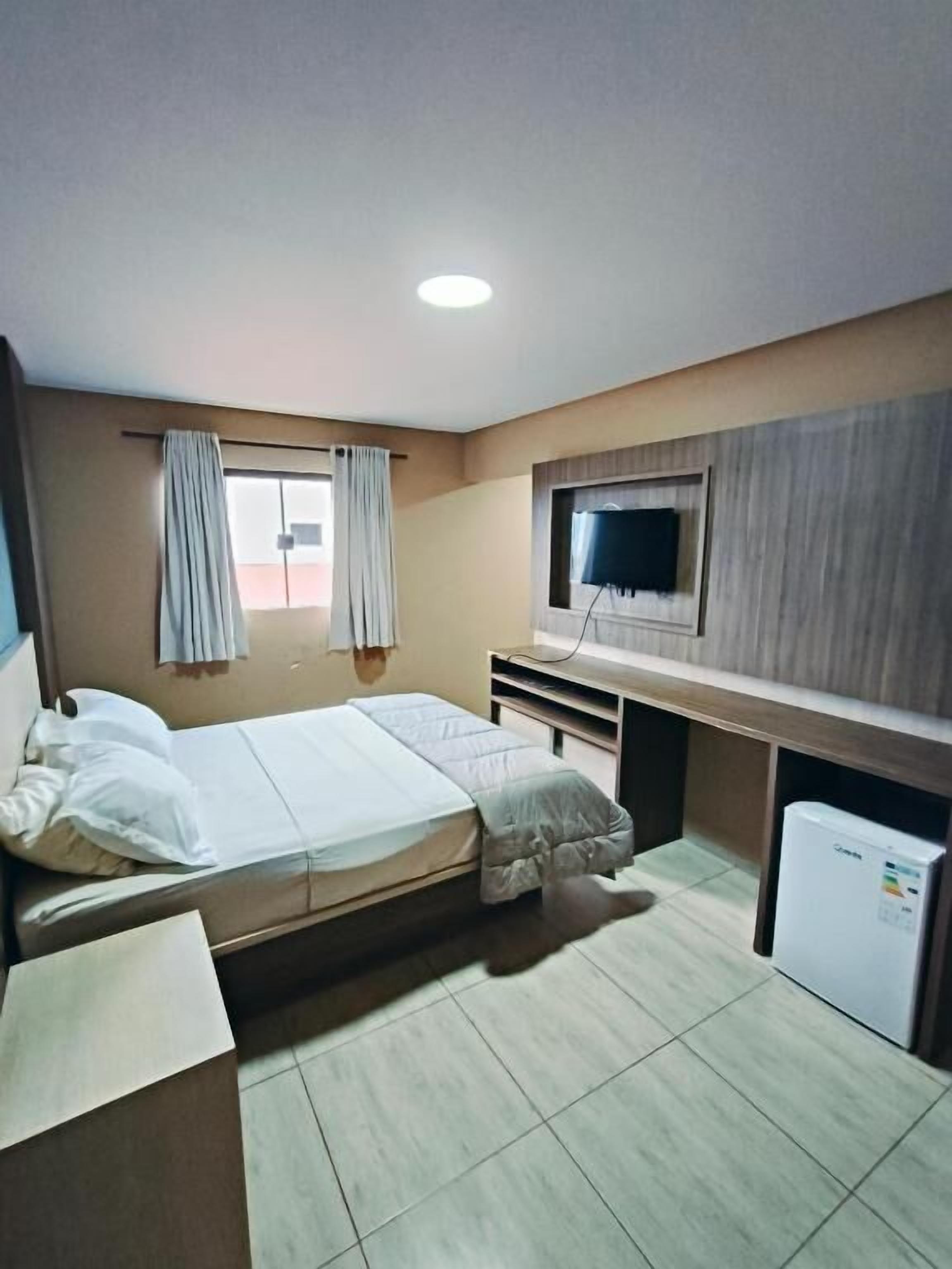 A hotel room with a bed, a desk, a television, and a small refrigerator.