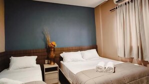 A hotel room with two beds, a nightstand, a vase with flowers, and an air conditioning unit. - Hotel Cardinal Pedro Juan Caballero (Pedro Juan Caballero)