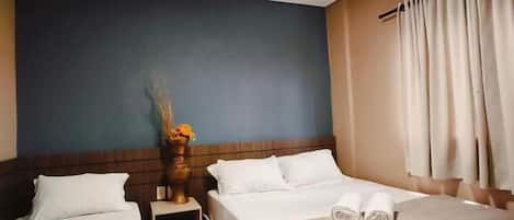 Quarto de hotel com duas camas, uma mesa de cabeceira, um vaso com flores e um ar condicionado.