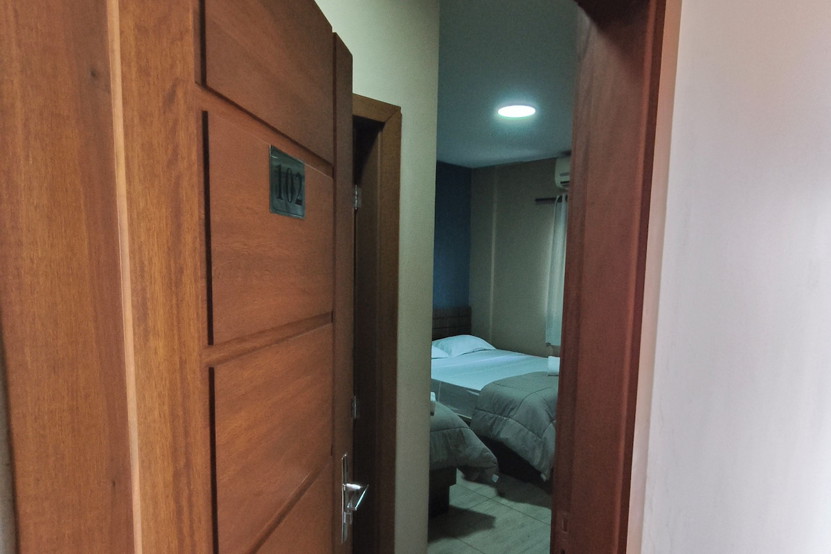 Una puerta de madera con una placa de número, que da paso a una habitación con una cama y una mesita de noche.